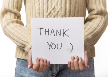 10 benefits of gratitude Lady holding up cards with 'Thank You' handwritten in black marker and a smiley face, symbolizing gratitude.