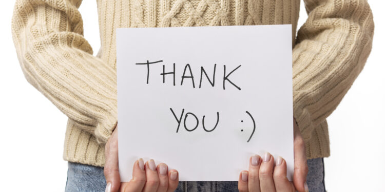 10 benefits of gratitude Lady holding up cards with 'Thank You' handwritten in black marker and a smiley face, symbolizing gratitude.