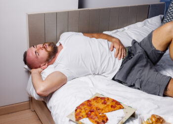 Man bed overeating fast food pizza