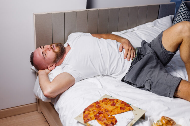 Man bed overeating fast food pizza