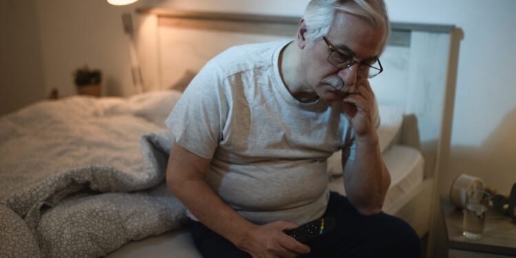 Mature man sitting in bed, wishing he knew how to fall asleep fast