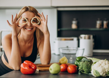 Young sporty woman in the kitchen, holding fresh peppers, highlighting the Gut Health Energy Connection and nutritious eating