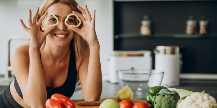 Young sporty woman in the kitchen, holding fresh peppers, highlighting the Gut Health Energy Connection and nutritious eating