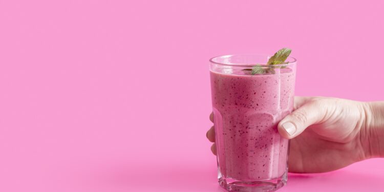Hand holding a glass of pink Herbalife smoothie with mint and copy-space